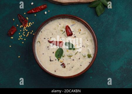 Vue de dessus d'un bol en bois plein de raitha ou de pachadi, plat de côté sud de l'Inde à base de papaye placé sur une texture vert foncé avec piment rouge sec et cu Banque D'Images