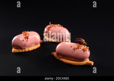 Gâteaux roses décorés de fleurs de rose sèches et de noix. Dessert à surface lisse, mousse et glaçage miroir sur biscuit isolé sur fond noir studio. Délicieux plat sucré à la cafétéria. Banque D'Images