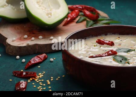 Papaye verte fraîche, dénoyautée en deux morceaux et disposée sur un morceau de bois avec du piment rouge sec et des feuilles de curry à côté et un bol en bois plein de r Banque D'Images