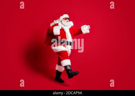 Pleine photo de profil de vieux vieux homme de la barbe grise marche sac ours cadeau responsable grand-père dépêchez-vous avant minuit lunettes de soleil de costume de père noël Banque D'Images