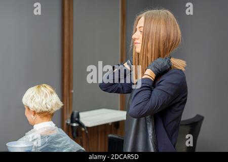 Le coiffeur féminin met un tablier noir avant de couper le client cheveux Banque D'Images