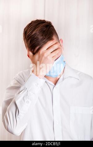 Triste jeune homme dans la grippe masque par le mur dedans La chambre Banque D'Images