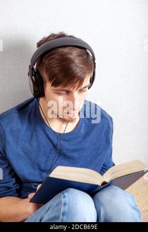 Un jeune homme dans un casque lit un livre à la maison Banque D'Images
