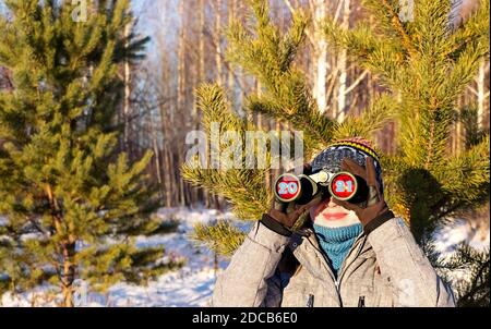 nouvelle année 2021 et concept de noël à venir. Jeune femme en bonnet tricoté et écharpe regardant à travers des jumelles avec les numéros 2021 dans les oculaires en hiver Banque D'Images