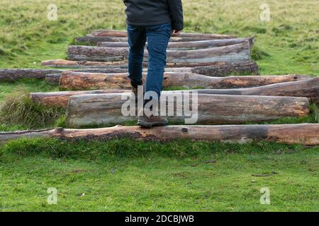 gros plan sur les jambes et les pieds de l'homme en marche sur les rondins de tronc d'arbre en bois à l'extérieur, portant des bottes de randonnée. Homme marchant à l'extérieur en faisant de l'exercice en hiver Banque D'Images