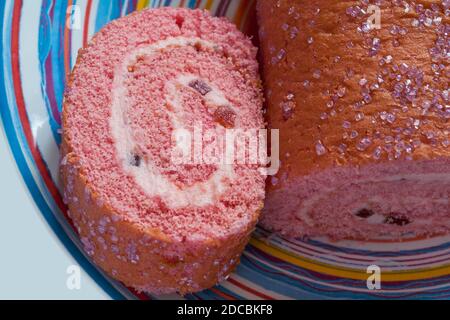 Coupez en tranches le gâteau au rouleau éponge M&S Percy Pig Sur plaque - rouleau d'éponge rose rempli de Percy Pig crème au beurre et morceaux de gelée moelleux Banque D'Images