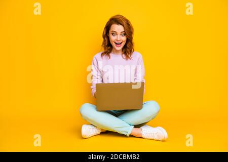 Pleine taille photo surprise fille assis pieds de sol pliés croisés ordinateur de travail lire les informations regarder la vidéo appel communiquer avec des amis portez un look élégant Banque D'Images