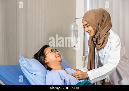 Femme musulmane médecin utilisant le stéthoscope pour écouter le battement de coeur, patient allongé sur le lit Banque D'Images