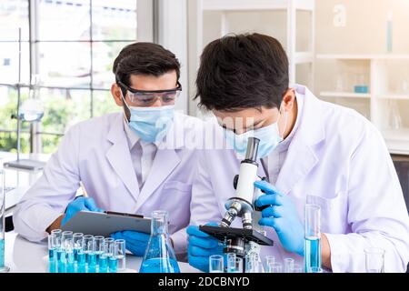 Deux chercheurs scientifiques asiatiques et arabes de sexe masculin travaillant en laboratoire, menant des études sur les substances à risque biologique à l'aide d'équipements scientifiques et d'un microscope Banque D'Images