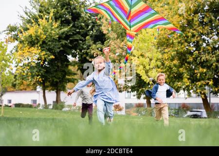 Fille souriante tenant le cerf-volant tout en jouant avec les garçons arrière-plan flou dans le parc Banque D'Images