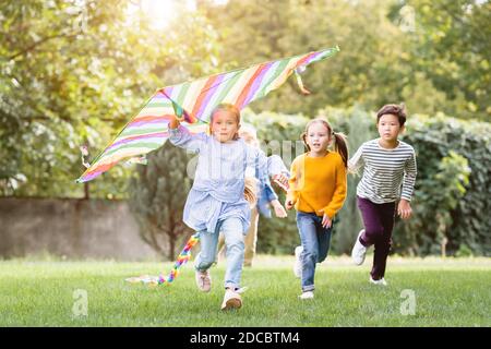 Jeune fille tenant un cerf-volant tout en courant près d'amis multiethniques dedans stationnement Banque D'Images
