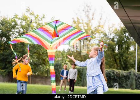 Fille tenant un cerf-volant coloré près d'amis sur un arrière-plan flou dans le parc Banque D'Images