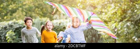 Fille avec cerf-volant courant près d'amis multiethniques dans le parc, bannière Banque D'Images