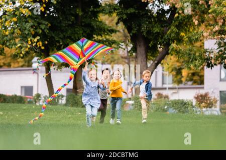 Des enfants multiethniques souriants qui s'amusent sur la pelouse en volant cerf-volant dans le parc Banque D'Images