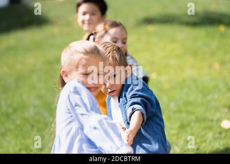 Garçon tirant la corde tout en jouant le remorqueur de la guerre avec des amis sur un premier plan flou dans le parc Banque D'Images