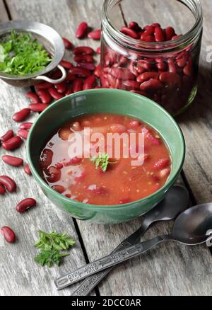 Haricots rouges cuits dans la sauce tomate garni de persil dans un bol vert sur table rustique en bois, gros plan, concept alimentaire sain de protéines végétaliennes Banque D'Images