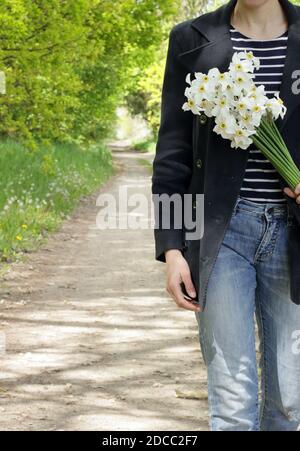 Femme habillée décontractée marchant dans la nature sauvage avec un bouquet de jonquilles, récolte, gros plan, espace de copie, connexion au concept de vie sauvage Banque D'Images