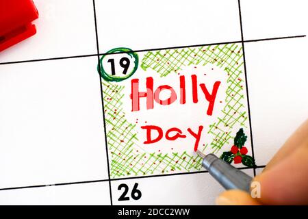 Femme doigts avec stylo écriture rappel Holly Day dans le calendrier. Décembre 19 Banque D'Images