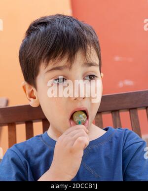 Concept d'enfance heureuse. Coupez un petit garçon mangeant des bonbons à la lylipop et s'amusant à l'extérieur Banque D'Images