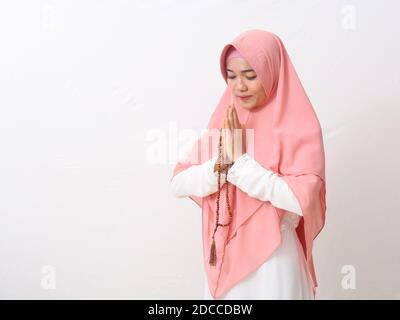 Une femme asiatique en robe musulmane se dresse dans une posture accueillante aux mains de Namaste, accueillant des invités, salutation EEI Fitr tout en tenant une perle de prière. Isola Banque D'Images