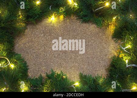 Cadre de branches de conifères avec des lumières jaunes sur un panneau en bois. Noël Banque D'Images