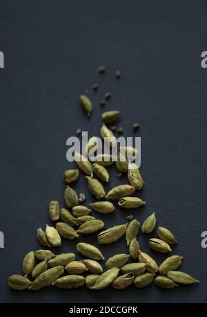 Photo verticale de petits DOF gros plan des gousses de Cardamom et des grains de la pile sur le fond noir mat. Il est très populaire dans la cuisine indienne et Sri Lanka. Banque D'Images