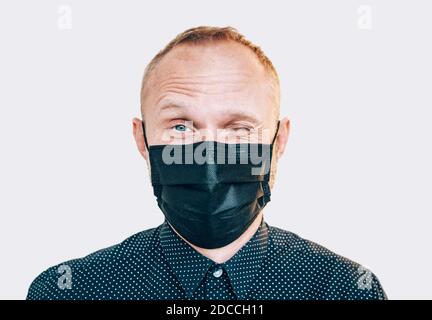 Portrait d'un drôle d'homme en forme de wencing dans un masque facial noir lors d'une pandémie mondiale COVID-19 regardant la caméra. Mesure d'auto-protection et d'arrêt de la propagation du virus Banque D'Images