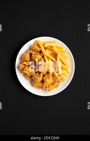 Beignets de poulet et frites faits maison sur une assiette sur fond noir, vue du dessus. Pose à plat, en hauteur, par le dessus. Banque D'Images