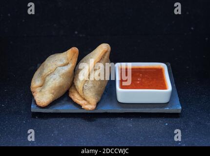 Samosa moderne servi avec une sauce chaude rouge sur un gris et un fond en marbre foncé Banque D'Images