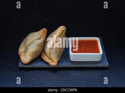 Samosa moderne servi avec une sauce chaude rouge sur un gris et un fond en marbre foncé Banque D'Images