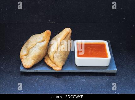 Samosa moderne servi avec une sauce chaude rouge sur un gris et un fond en marbre foncé Banque D'Images