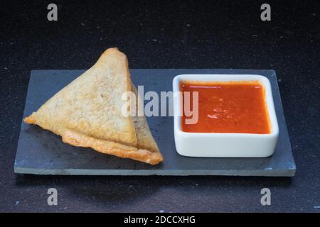 Samosa moderne servi avec une sauce chaude rouge sur un gris et un fond en marbre foncé Banque D'Images