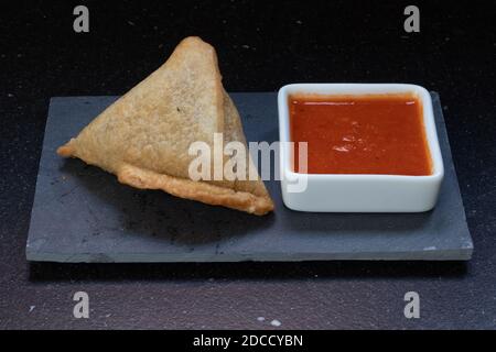 Samosa moderne servi avec une sauce chaude rouge sur un gris et un fond en marbre foncé Banque D'Images