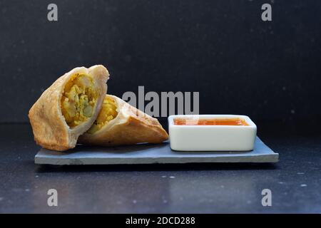 Samosa moderne servi avec une sauce chaude rouge sur un gris et un fond en marbre foncé Banque D'Images