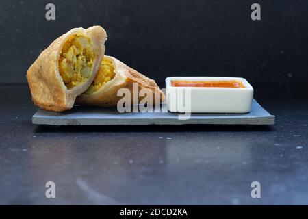 Samosa moderne servi avec une sauce chaude rouge sur un gris et un fond en marbre foncé Banque D'Images