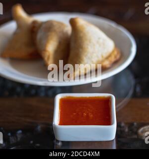 Samosas sur une assiette blanche avec sauce rouge épicée Banque D'Images