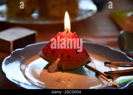 Bougie fondue en forme de triangle de melon d'eau. Flamme aux chandelles en gros plan. Feu de bougie sur plaque d'époque avec allumettes brûlées à proximité Banque D'Images