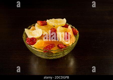 Tranches de melon confites jaunes, anneaux d'ananas et cornouiller dans un vase en verre sur fond noir. Banque D'Images