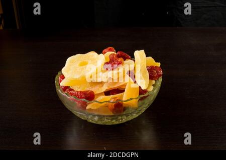 Tranches de melon confites jaunes, anneaux d'ananas et cornouiller dans un vase en verre sur fond noir. Banque D'Images