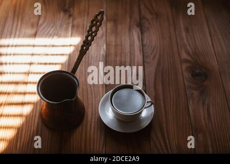 Café aromatique chaud dans une tasse en porcelaine blanche sur une soucoupe sur une table en bois le matin. Café turc traditionnel préparé dans un cof turc en cuivre Banque D'Images