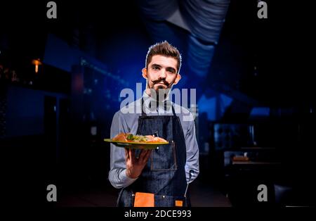 Le serveur charismatique sert une assiette avec un plat préparé dans le restaurant. Banque D'Images