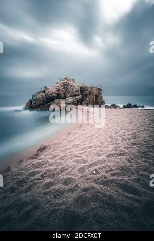 Longue exposition de ciel dramatique avec roche solitaire sur la plage de Sant Pol de Mar, Catalunya, Espagne Banque D'Images