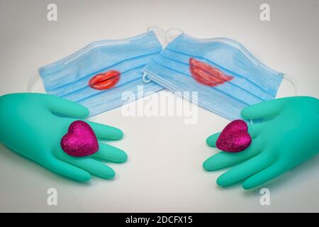 Il y a deux masques médicaux avec des lèvres rouges peintes sur eux. Au premier plan se trouvent des gants médicaux verts, chacun portant un cœur écarlate. Mise au point sélective Banque D'Images