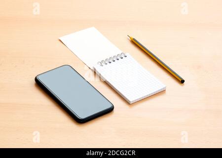 Un bloc-notes vierge en spirale avec un stylo et un smartphone sont disposés sur une table en bois. Concept de liste à faire pendant l'épidémie de Covid-19. Banque D'Images