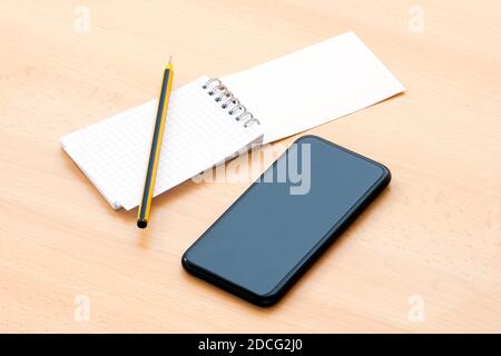 Un bloc-notes vierge en spirale avec un stylo et un smartphone sont disposés sur une table en bois. Concept de liste à faire pendant l'épidémie de Covid-19. Banque D'Images