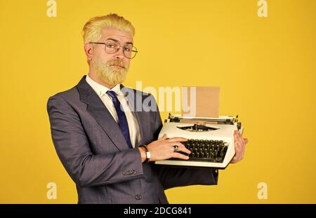 Objets vendeurs vintage. Homme mature teint cheveux cheveux fond jaune. Magasin de produits d'occasion. Connaisseur des valeurs millésières. Machine à écrire vintage. L'écrivain colle de vieilles habitudes. Les hommes d'affaires utilisent la technologie rétro. Banque D'Images