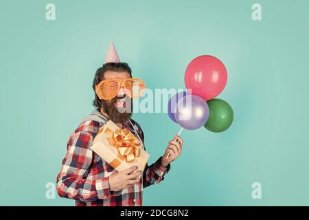 Quoi acheter. Gestionnaire d'événements avec boîte cadeau. Homme brutal en fête. Homme drôle en chapeau d'anniversaire. Joyeux Noël. Fête de la fête, fou. S'amuser avec des ballons. Préparez-vous pour un anniversaire. Banque D'Images