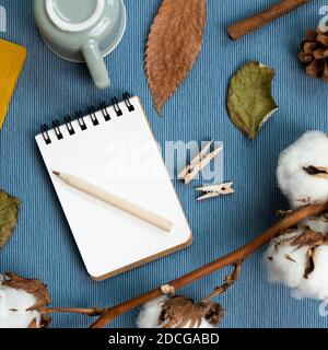 Lieu de travail et d'étude. Concept d'hiver. Carnet et crayon, tasse à café, plante sèche sur fond de tissu bleu. pose à plat, vue du dessus, espace de copie Banque D'Images