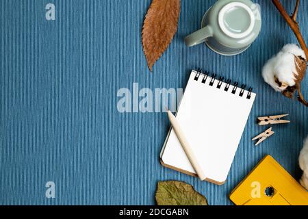 Lieu de travail et d'étude. Concept d'hiver. Carnet et crayon, tasse à café, plante sèche sur fond de tissu bleu. pose à plat, vue du dessus, espace de copie Banque D'Images