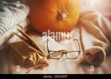 Sur le lit doux se trouve une pile de chandails chauds, une grande citrouille, des verres, un livre ouvert, et des feuilles d'érable sèches. Décorations pour les vacances. Récolte. Accueil c Banque D'Images